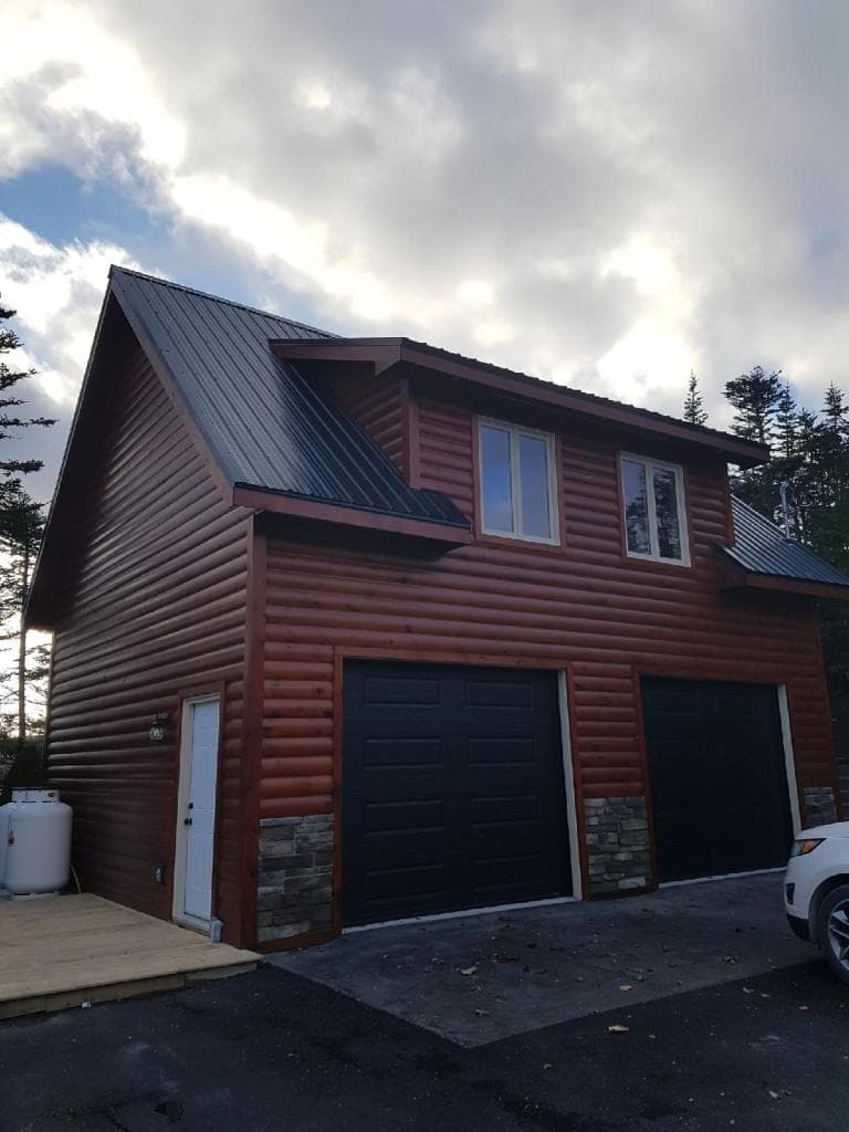 Two-story detached garage with log siding, black doors and black metal roof