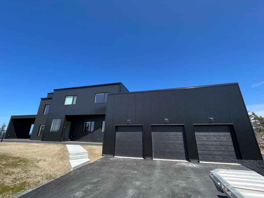 Modern architectural estate with full black vertical metal siding and 3 garage bays